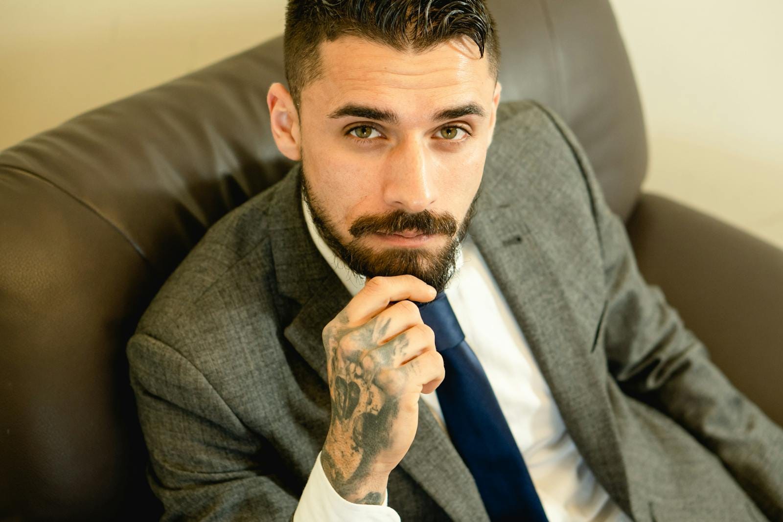 Portrait of a bearded businessman with formal attire sitting confidently indoors.